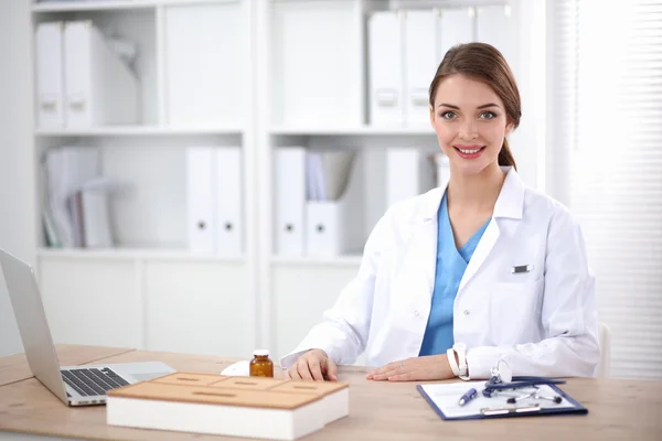Kadın doktor masada oturuyor ve hastanede dizüstü bilgisayarla çalışıyor. — Stok fotoğraf