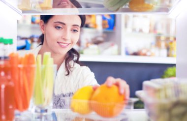 Sağlıklı yiyecek, sebze ve meyvelerle dolu açık buzdolabının yanında duran kadın portresi.