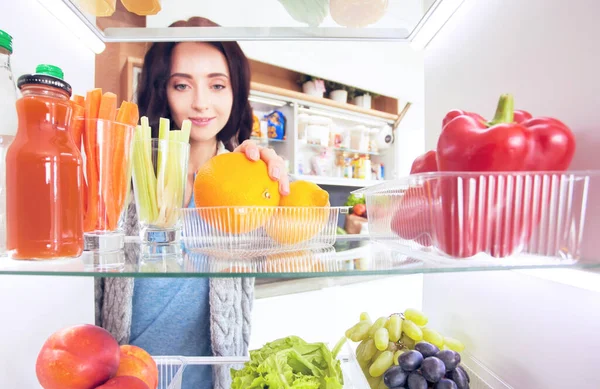 Portrait of female standing near open fridge full of healthy food, vegetables and fruits — Stock Photo, Image