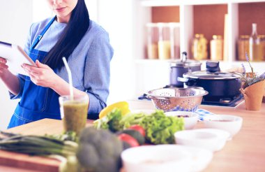 Mutfakta yemek yapmak için tablet bilgisayar kullanan genç bir kadın.