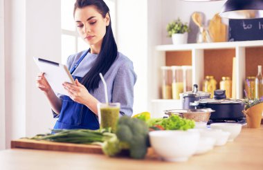 Mutfakta yemek yapmak için tablet bilgisayar kullanan genç bir kadın.