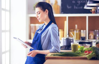Mutfakta yemek yapmak için tablet bilgisayar kullanan genç bir kadın.