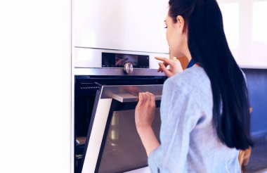 Güzel genç bayan pastasının fırında ne yaptığını kontrol ediyor.