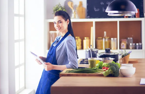 Mujer joven usando una tableta para cocinar en su cocina — Foto de Stock