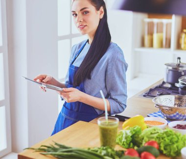 Mutfakta yemek yapmak için tablet bilgisayar kullanan genç bir kadın.
