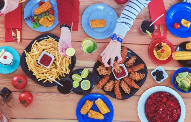 Ahşap masada otururken birlikte yemek yiyen bir grup insanın üst düzey görüntüsü. Masada yemek var. İnsanlar fast food yiyor..