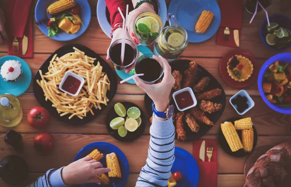 Ahşap masada otururken birlikte yemek yiyen bir grup insanın üst düzey görüntüsü. Masada yemek var. İnsanlar fast food yiyor..