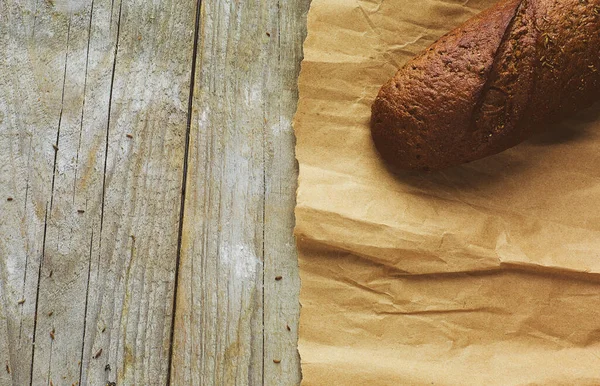 Tahta masanın üzerinde kağıda sarılı bir somun ekmek.. — Stok fotoğraf