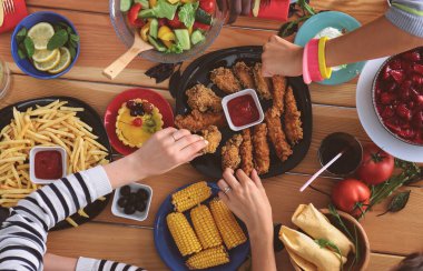Ahşap masada otururken birlikte yemek yiyen bir grup insanın üst düzey görüntüsü. Masada yemek var. İnsanlar fast food yiyor..