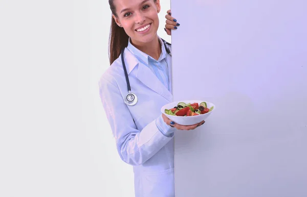 一个美丽的女医生的肖像拿着盘子, 新鲜蔬菜站在空白附近。女医生 — 图库照片