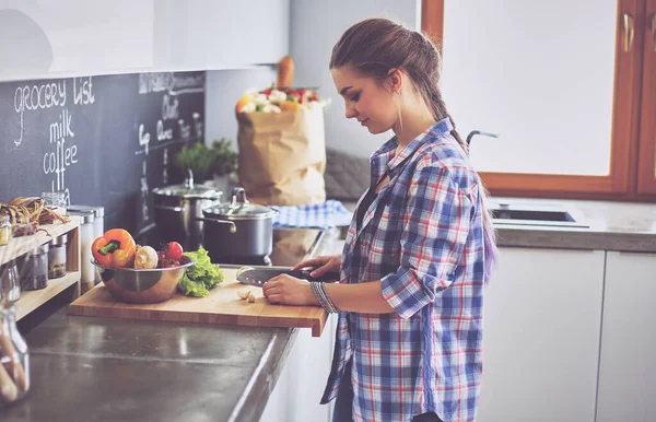 Junge Frau schneidet Gemüse in Küche neben Schreibtisch — Stockfoto