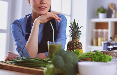 Mutfaktaki masada bir bardak lezzetli, sağlıklı smoothie ile genç bir kadın.