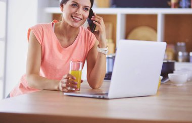 Mutfakta dizüstü bilgisayara benzeyen tariflerle gülümseyen genç bir kadın. Gıda blogcusu kavramı