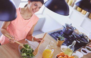 Gülümseyen genç kadın mutfakta taze salata karıştırıyor..
