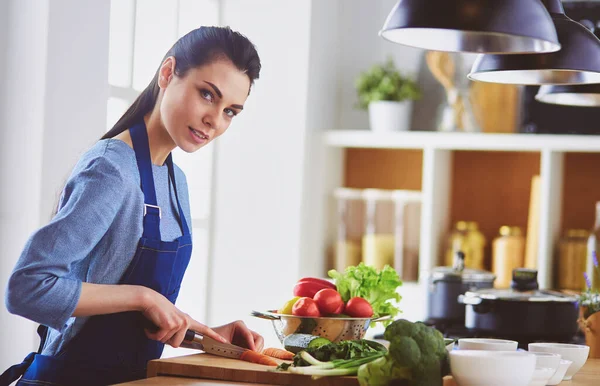 Ung kvinna skära grönsaker i köket hemma — Stockfoto