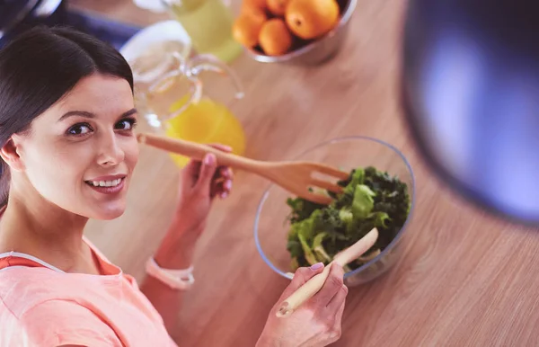 Giovane donna sorridente che mescola insalata fresca in cucina. — Foto Stock