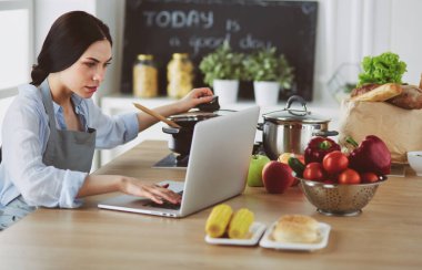 Mutfakta dizüstü bilgisayara benzeyen tariflerle gülümseyen genç bir kadın. Gıda blogcusu kavramı