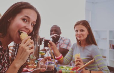 Ahşap masada otururken birlikte yemek yiyen bir grup insanın üst düzey görüntüsü. Masada yemek var. İnsanlar fast food yiyor..