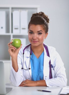 Kadın doktor, elinde yeşil bir elma, oturuyor.