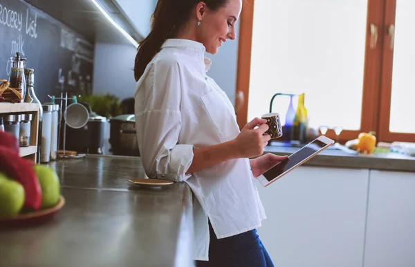 Fiatal nő használja tabletta a konyhában otthon és kávézás — Stock Fotó