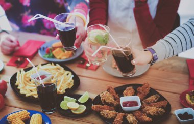 Ahşap masada otururken birlikte yemek yiyen bir grup insanın üst düzey görüntüsü. Masada yemek var. İnsanlar fast food yiyor..