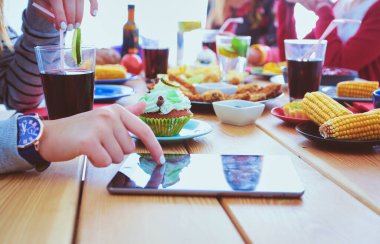 Ahşap masada otururken birlikte yemek yiyen bir grup insanın üst düzey görüntüsü. Masada yemek var. İnsanlar fast food yiyor..