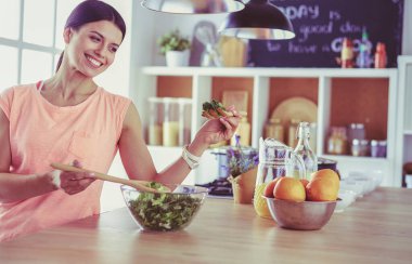 Gülümseyen genç kadın mutfakta taze salata karıştırıyor..