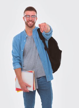 Okul kitapları tutarak ve beyaz arka plan üzerinde izole işaret eden çantası ile genç erkek öğrenci