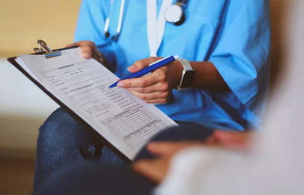 Женщина-врач держит серебряную ручку, заполняя список пациентов в блокноте — стоковое фото