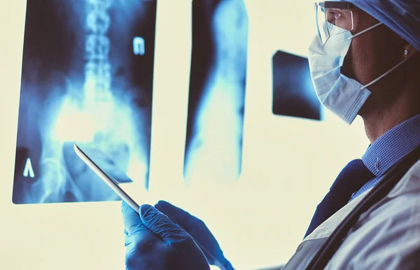 Médico en el hospital sentado en el escritorio mirando los rayos X en la tableta contra el fondo blanco con rayos X — Foto de Stock