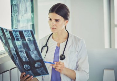 Stetoskop lu genç gülümseyen kadın doktor doktor ofisinde röntgeni işaret ediyor