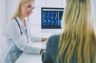 Hasta bir tıbbi Danışma alma ve kameraya bakarak gülen, kadın doktor masada oturuyor.