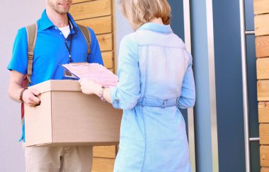 Mavi üniformalı gülümseyen kurye servis konseptine paket kutusu teslim eden teslimatçı. Mavi üniformalı gülümseyen teslimatçı..