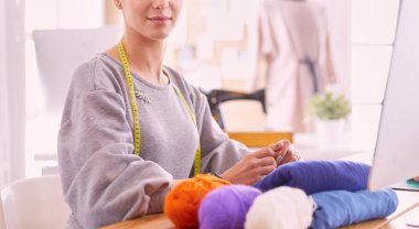 Moda tasarımcısı kadın stüdyoda çalışıyor, masada oturuyor..