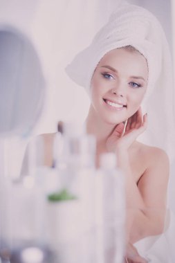 Bornozlu genç kadın banyo aynasına bakıyor..