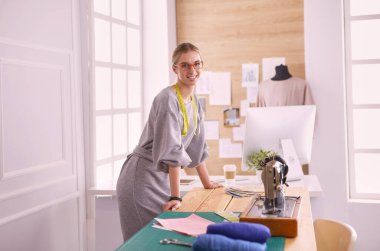 Yeni moda tarzlar yaratıyor. Moda atölyesinde çalışırken dikiş diken neşeli genç bir kadın..