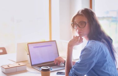 Ofis masasında oturan genç bir kadın dizüstü bilgisayar ekranına bakıyor. Genç kadın..