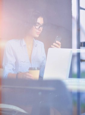 Ofis masasında dizüstü bilgisayarıyla oturan genç bir kadın. Pencereden bakıyor. Genç kadın..