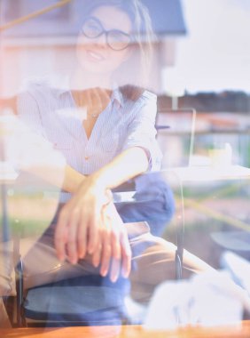 Ofis masasında dizüstü bilgisayarıyla oturan genç bir kadın. Pencereden bakıyor. Genç kadın..