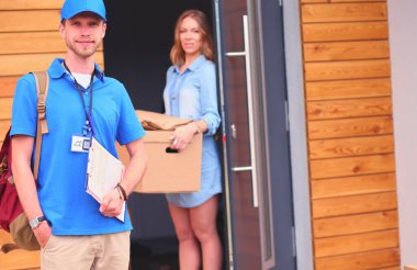 Mavi üniformalı gülümseyen kurye servis konseptine paket kutusu teslim eden teslimatçı. Mavi üniformalı gülümseyen teslimatçı..