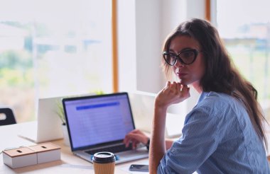 Ofis masasında oturan genç bir kadın dizüstü bilgisayar ekranına bakıyor. Genç kadın..