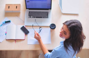 Ofis masasında oturan genç bir kadın dizüstü bilgisayar ekranına bakıyor. Genç kadın..