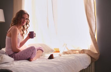 Dizüstü bilgisayar ile yatakta oturan genç güzel kadın