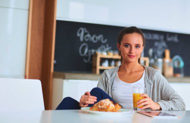 Mutfakta portakal suyu ve tableti olan genç bir kadın..