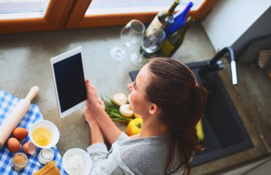 Tablette tarifi takip eden bir kadın evde yemek pişiriyor..