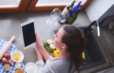Güzel bir kadın mutfakta pasta pişiriyor. Masanın yanında duruyor.