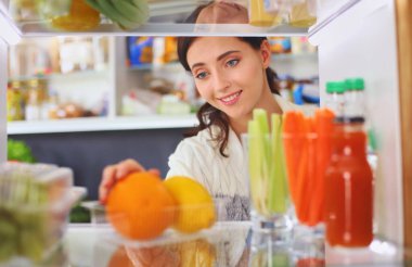 Sağlıklı yiyecek, sebze ve meyvelerle dolu açık buzdolabının yanında duran kadın portresi. Kadın portresi.