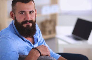 dizüstü bilgisayar ve bir çay bardağı evde oturan genç adam.