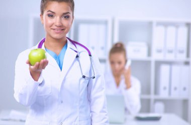 Kadın doktor, elinde yeşil bir elma, oturuyor..