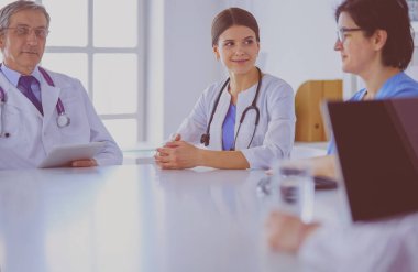 Ciddi bir tıbbi ekip parlak bir ofiste dizüstü bilgisayar kullanıyor.